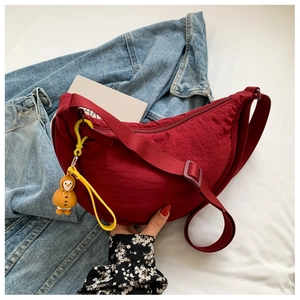 Detail of red crescent nylon bag with yellow duck charm on blue denim backdrop