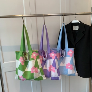 Knit tote bags with checkered floral patterns in green, purple, and blue hanging on rack