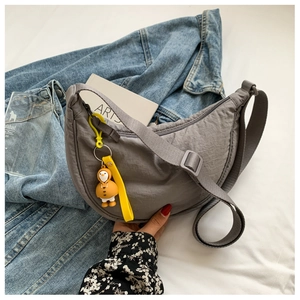 Close-up of a dark grey nylon crescent bag with a cute duck charm on a street style background