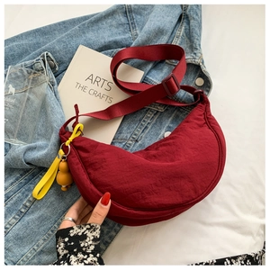 Deep red nylon crescent crossbody bag with yellow bear charm on denim jacket background