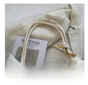 Detail of cream tweed bag showing round rope shoulder strap and metal ring knot