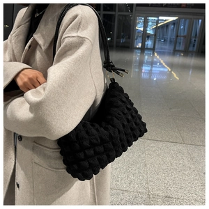 Detail of black bubble textured fabric shoulder bag with leather strap on grey coat