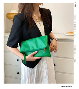 Detalle de bolso sobre plegado verde brillante con cremallera dorada y asa de cuero
