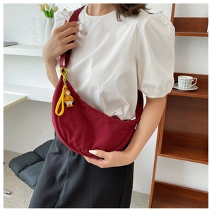 Deep red canvas crescent crossbody bag worn by model, featuring a cute yellow duck pendant