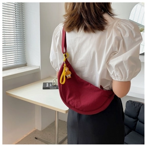 Detail of burgundy crescent crossbody bag with cute yellow duck pendant on a female model