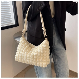 Detail of ruched texture and metal ring buckle on a beige shoulder bag worn with a suit
