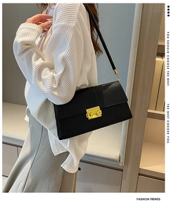 Detail of black stone textured leather shoulder bag with golden lock on a model