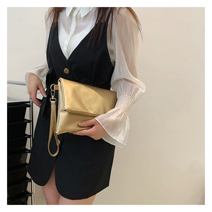 Detalle de bolso sobre dorado metalizado con correa de muñeca desmontable y cierre plegable
