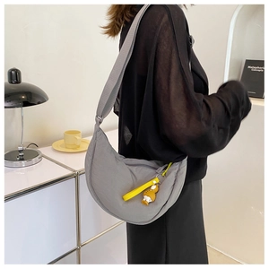 Nylon half-moon crossbody bag in grey with a bright yellow zipper pull and cartoon charm