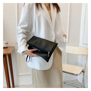 Elegante bolso de sobre en cuero negro con cremallera dorada sostenido por una modelo