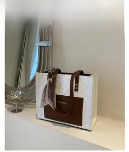 Detail of woven tote bag featuring brown leather trim and silk scarf on handle
