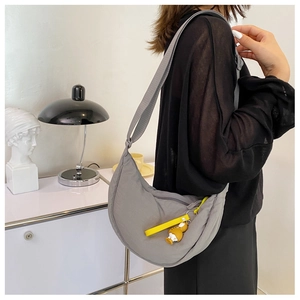 Grey nylon crescent bag detail featuring a wide strap and yellow doll keychain
