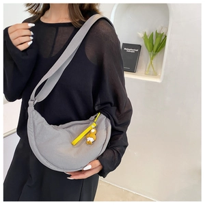 Close-up of grey nylon crescent bag with yellow strap and charm on a female model
