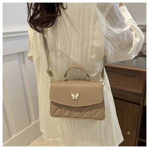 Beige quilted crossbody bag with butterfly buckle shown on model in modern room