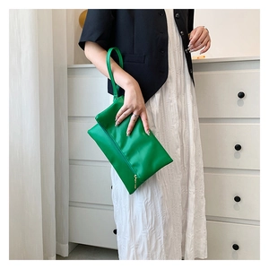 Detalle de bolso sobre de cuero verde brillante con correa de mano y cremallera dorada