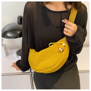 Detail of a vibrant yellow crescent nylon crossbody bag with a cute duck charm on a model