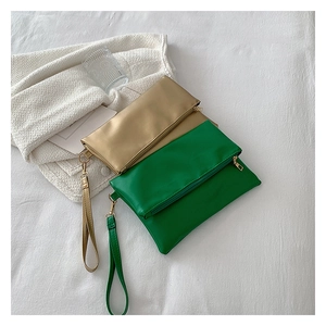 Bolsos de mano tipo sobre en verde y champán con correas de muñeca sobre tela blanca