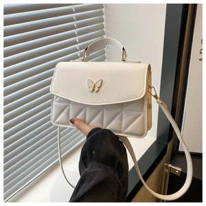 Close-up of white quilted crossbody bag featuring a decorative metal butterfly clasp