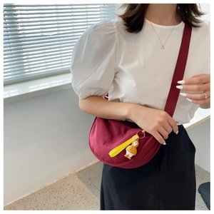 Detail of burgundy crescent crossbody bag with yellow cartoon duck charm on nylon strap