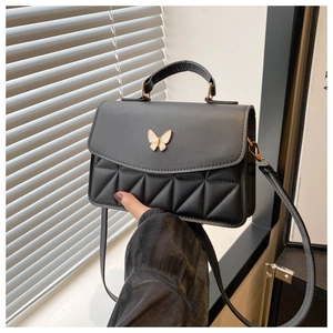 Detail of black quilted shoulder bag featuring elegant gold butterfly clasp and textures