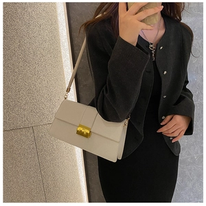 Close-up of ivory flap crossbody bag with a gold rectangular metal buckle on a model