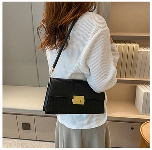 Detailed view of black crocodile pattern leather bag with elegant gold twist lock