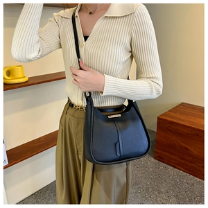 Sac hobo chic en cuir noir mat avec détails dorés porté avec une tenue décontractée d'automne