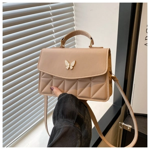Detail of apricot quilted crossbody bag featuring a golden butterfly buckle and texture