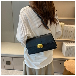 Detail of black faux crocodile leather bag with gold buckle on a model's shoulder