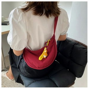 Detail of burgundy crescent nylon crossbody bag with a yellow duck pendant