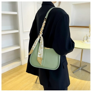 Détail d'un sac sous le bras vert clair avec foulard en soie et bandoulière dorée