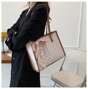Chic monogram tote bag with silk scarf detail worn over the shoulder in a minimalist setting