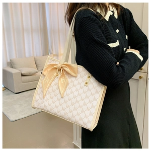 Detail of beige monogram tote bag featuring decorative silk scarf on shoulder strap