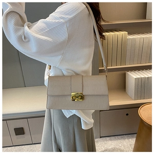 Detail view of cream shoulder bag with crocodile texture and gold metal square clasp