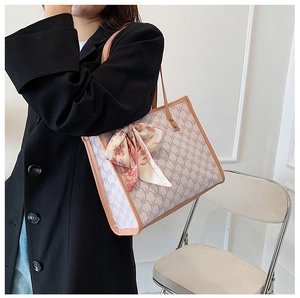 Close-up of a large printed tote bag with NK monogram and a decorative silk scarf on handle