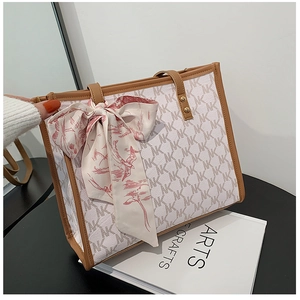 Detail view of cream monogram tote bag with brown leather handles and a silk scarf accent