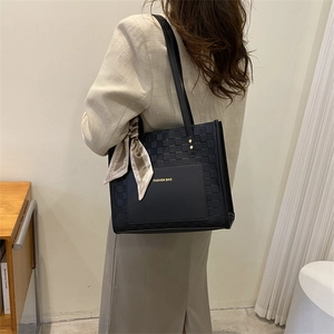 Black leather tote bag with woven pattern and floral scarf handle on a female model