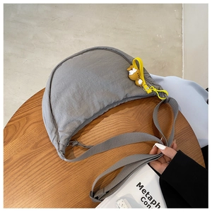 Detailed view of gray nylon crescent bag with yellow strap and charm on wooden table