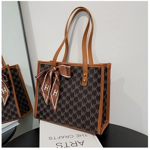 Detail of monogram tote bag with brown leather handles and a decorative silk bow scarf