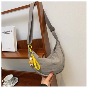 Detail of grey nylon half-moon crossbody bag with cute yellow duck pendant on a desk