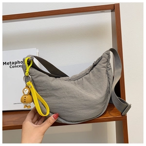 Detail of grey nylon crescent bag with textured fabric and yellow duck charm on shelf