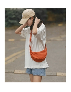 Outdoor shot of a bright orange half-moon nylon crossbody bag worn by a female model