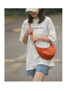 Outdoor street style view of a vibrant orange nylon crescent waist bag on a model
