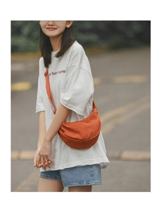 Outdoor shot of an orange half-moon crossbody bag with adjustable strap on a model