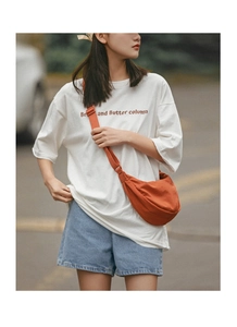 Outdoor shot of a model wearing a bright orange nylon crescent crossbody bag with casual outfit