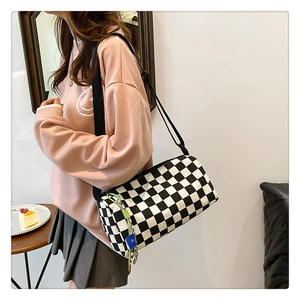 Nahaufnahme der Schachbrett-Zylindertasche mit dekorativem Anhänger am Model-Outfit