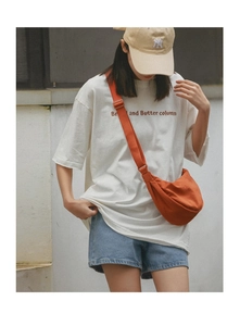 Detail of bright orange nylon crescent moon bag worn by model in casual street style