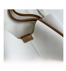 Detail shot of white leather tote bag featuring brown contrast handles and neat stitching