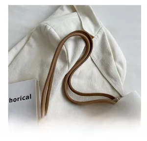 Detail of slim brown leather handle on a minimalist white tote bag with lifestyle setting