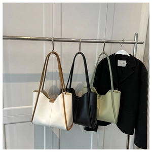 Three minimalist large tote bags in cream, black and green shown hanging on a metal rack